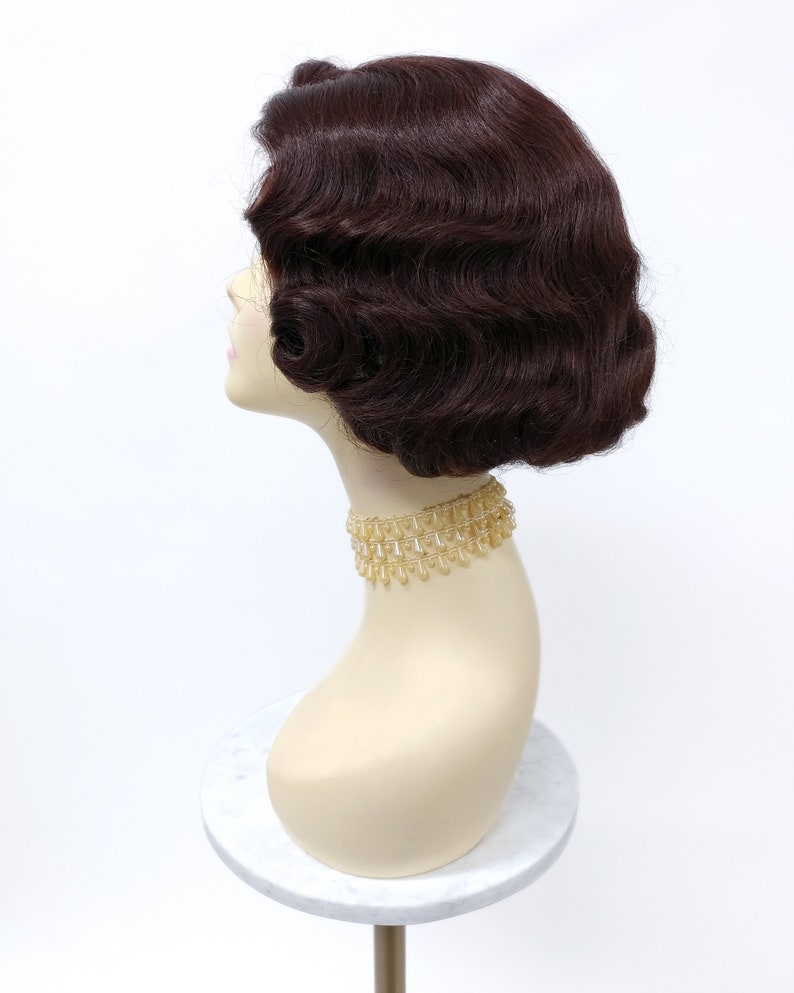 May include: A dark brown wig with a vintage style, featuring soft waves and a short bob cut. The wig is displayed on a mannequin head.