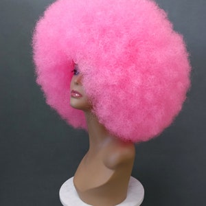 May include: A bright pink afro wig on a mannequin head. The wig is very large and fluffy.