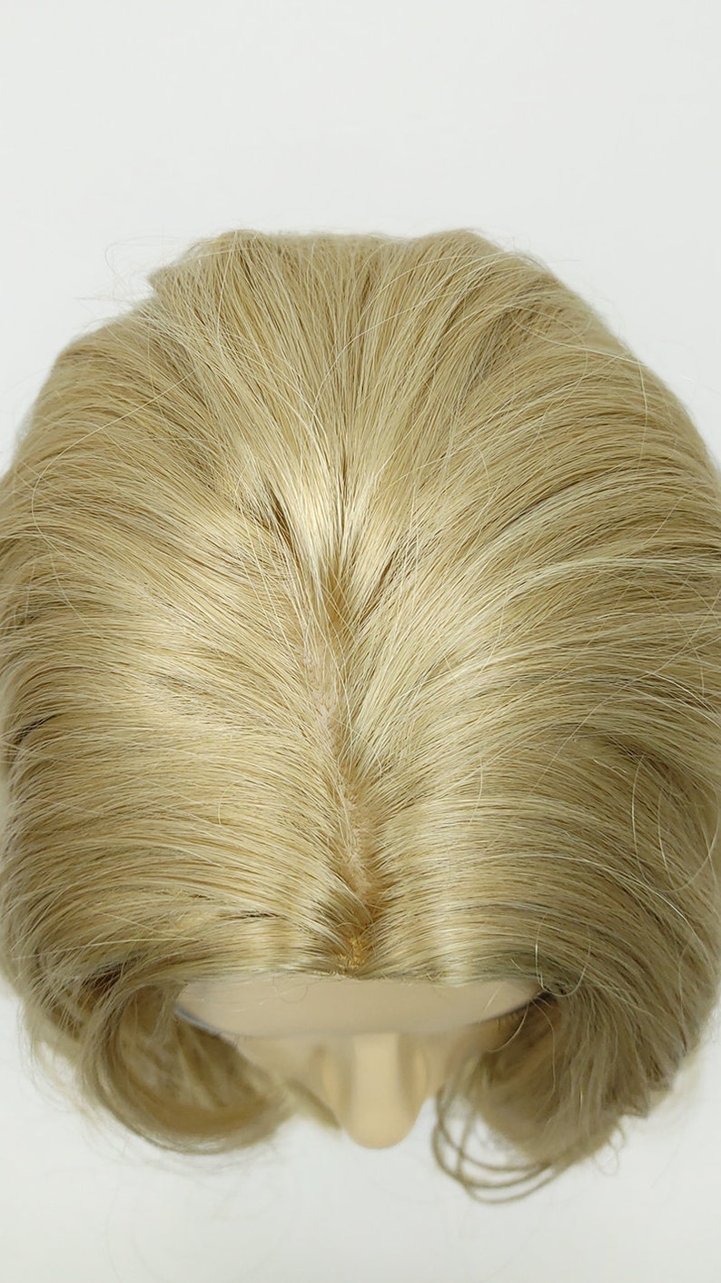 Peut inclure: Une perruque blonde clair avec un style droit et lisse. La perruque est sur une t&ecirc;te de mannequin et le dessus de la perruque est visible.