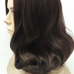 May include: A dark brown wig with shoulder-length, wavy hair. The wig is styled with a side part and features soft curls. The wig is displayed on a mannequin head against a white background. The wig's color is a rich, dark brown.