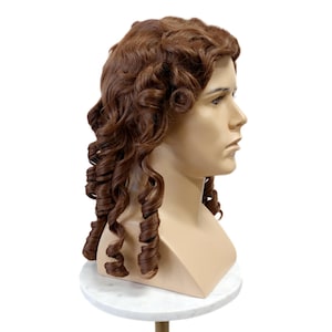 May include: A brown wig with long, voluminous curls, styled in a classic, historical fashion. The wig is displayed on a mannequin head, showcasing the intricate curl pattern and color. The mannequin is on a white marble stand.