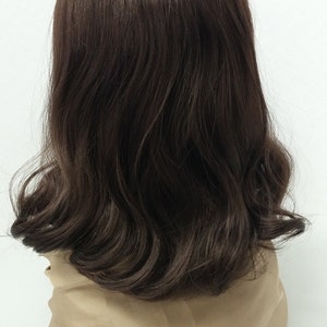 May include: A dark brown wig with wavy, shoulder-length hair. The wig has a natural-looking hairline and a slight ombre effect, with darker roots fading into lighter brown ends. The wig is displayed on a beige mannequin head against a white background.