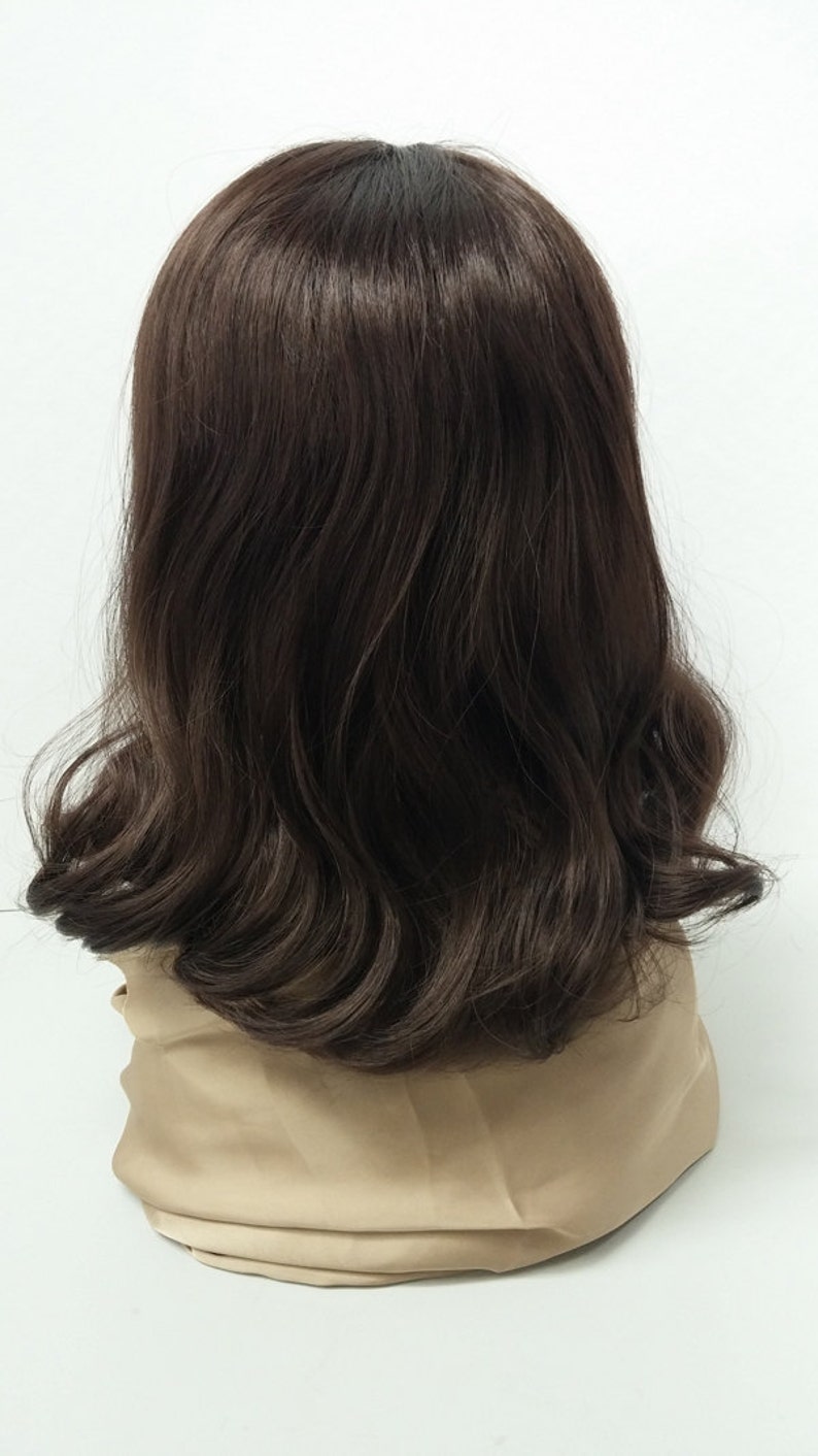 May include: A dark brown wig with wavy, shoulder-length hair. The wig has a natural-looking hairline and a slight ombre effect, with darker roots fading into lighter brown ends. The wig is displayed on a beige mannequin head against a white background.