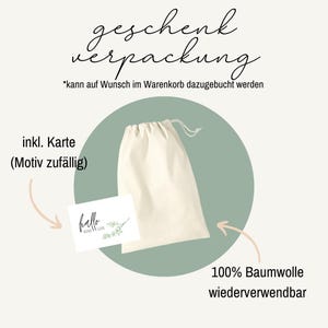 May include: A cream-colored drawstring bag and a small card with the word "hello" and a botanical illustration are displayed. Text in German reads "geschenk verpackung" (gift wrapping) and "100% Baumwolle wiederverwendbar" (100% cotton reusable).