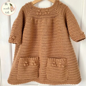 May include: A brown crocheted dress with 3/4 sleeves and two pockets. The dress has a round neckline and a textured pattern.