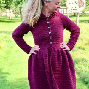 以下が含まれることがあります： フリルカラーとボタン留めのボルドー色のクロシェ編みドレス。ドレスはフィットしたボディとフレアスカートになっています。ドレスは、ポニーテールにしたブロンドの髪をした人が着用しています。画像には「The moule hole」というテキストが含まれています。