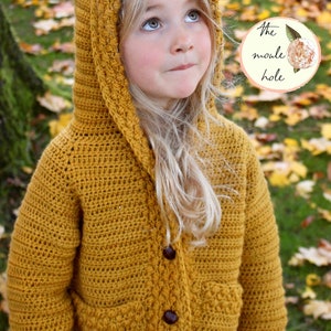 May include: A mustard yellow crocheted hooded cardigan with a button closure and pockets. The cardigan is made with a textured stitch and has a simple design.