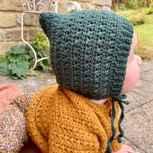 Puede incluir: Un beb&eacute; con un gorro de punto verde oscuro con un lazo y un su&eacute;ter de punto amarillo mostaza.