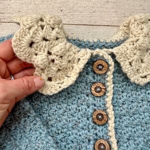 May include: A blue crocheted cardigan with a white crocheted collar and wooden buttons.