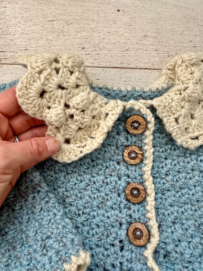 May include: A blue crocheted cardigan with a white crocheted collar and wooden buttons.