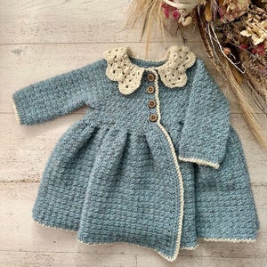 May include: A blue crocheted baby cardigan with a white crocheted collar and wooden buttons.