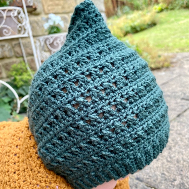 Puede incluir: Un gorro de punto de color azul verdoso con la parte superior puntiaguda y un dise&ntilde;o de encaje.