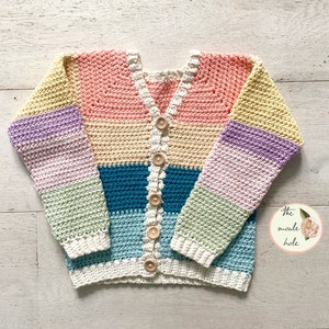 May include: A colorful striped crochet cardigan with wooden buttons. The cardigan is made in a variety of pastel colors, including pink, yellow, purple, green, and blue. The cardigan has a V-neck and long sleeves.