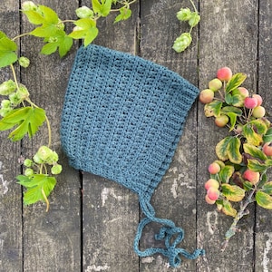 Puede incluir: Un gorro de beb&eacute; de ganchillo azul verdoso con un patr&oacute;n de punto sencillo. El gorro tiene lazos que se pueden atar debajo de la barbilla.