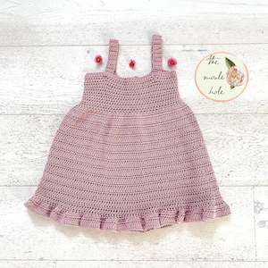 May include: A dusky pink crochet dress with a frilled hem and shoulder straps. The dress is handmade and features a textured stitch pattern. The image includes the text "the moule hole" in a circular logo with a floral design.