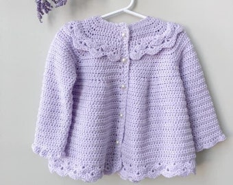 May include: A lavender crocheted cardigan with a scalloped collar and pearl buttons. The cardigan has a delicate crocheted design and is perfect for a baby or toddler.