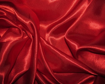 May include: A close-up of a smooth, red satin fabric with soft folds and wrinkles. The fabric has a subtle sheen and a luxurious feel.
