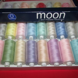 May include: A box of Coats Moon Spun Polyester thread in a variety of pastel colors. The box is blue with the Coats logo and the words "Moon Spun Polyester Assortment".