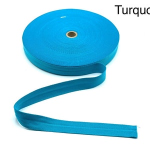 May include: A turquoise ribbon with a herringbone weave. The ribbon is rolled up and a length of the ribbon is extended.