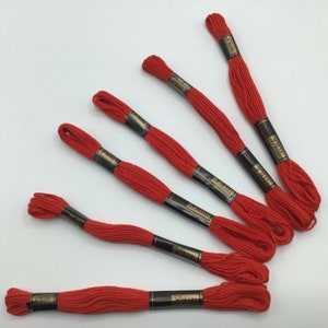 May include: Six spools of red embroidery floss with black labels and gold lettering. The labels read "DMC Cotton Embroidery Floss".