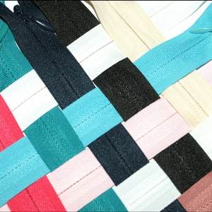 May include: A selection of zipper tapes in various colours, including red, pink, white, black, teal and beige. The tapes are woven together in a grid pattern.