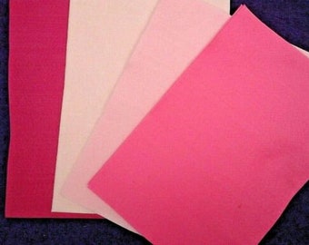 May include: An assortment of pink and white felt sheets displayed on a dark blue background. The felt ranges in colour from deep magenta to pale blush, with one white sheet. The sheets are arranged to create a layered effect.