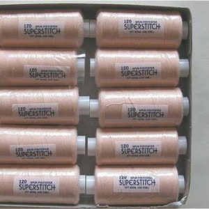 May include: A box containing peach-coloured thread spools. Each spool has a white label with the text "120 SUPERSTITCH". The spools are neatly arranged in rows within a cardboard box, suitable for sewing.