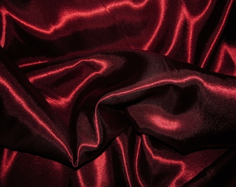 May include: Close-up of a deep red satin fabric with soft, flowing folds and a luxurious sheen.