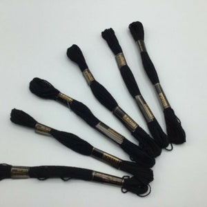 May include: Six spools of black embroidery floss, each with a gold label.