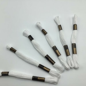 May include: Six spools of white embroidery floss with black and gold labels that read "Iberla".