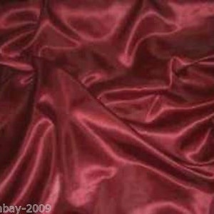 Könnte beinhalten: Eine Nahaufnahme eines tief roten Satin-Stoffes mit einer glatten, seidenartigen Textur. Der Stoff ist drapiert und gefaltet, wodurch weiche, fließende Linien entstehen.