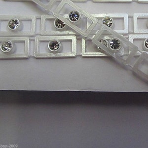 May include: A roll of clear plastic trim with small, clear rhinestones set in rectangular frames. The trim is designed for adding sparkle and embellishment to crafts and projects.