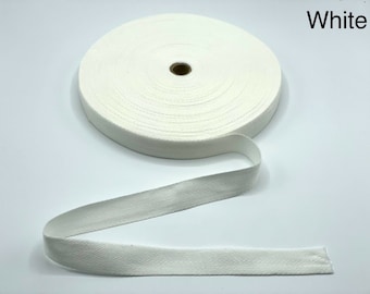 May include: A roll of white cotton twill tape with a herringbone pattern. The tape is wound around a cardboard spool.