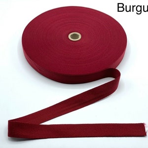 Könnte beinhalten: Eine Rolle burgunderfarbenes Baumwoll-Twillband mit Fischgrätenmuster. Das Band ist etwa 2,5 cm breit.