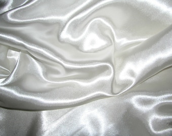 May include: White satin fabric with a smooth, silky texture. The fabric is draped and folded, creating soft, flowing lines.