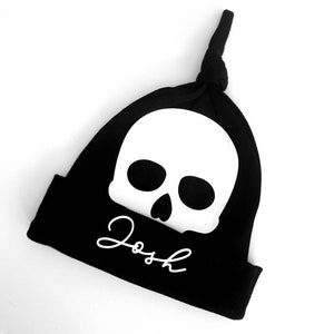 May include: Black knit beanie with a white skull and the name "Josh" written in white cursive.
