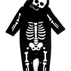 May include: Black skeleton costume with a white skeleton design. The costume includes a matching skull hat with the name "Josh" written on it.