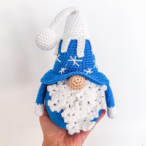 Peut inclure: Un gnome crocheté bleu et blanc fait à la main, avec une barbe et un chapeau blancs. Le chapeau du gnome présente des détails de flocons de neige. Le gnome mesure environ 15 cm de haut.