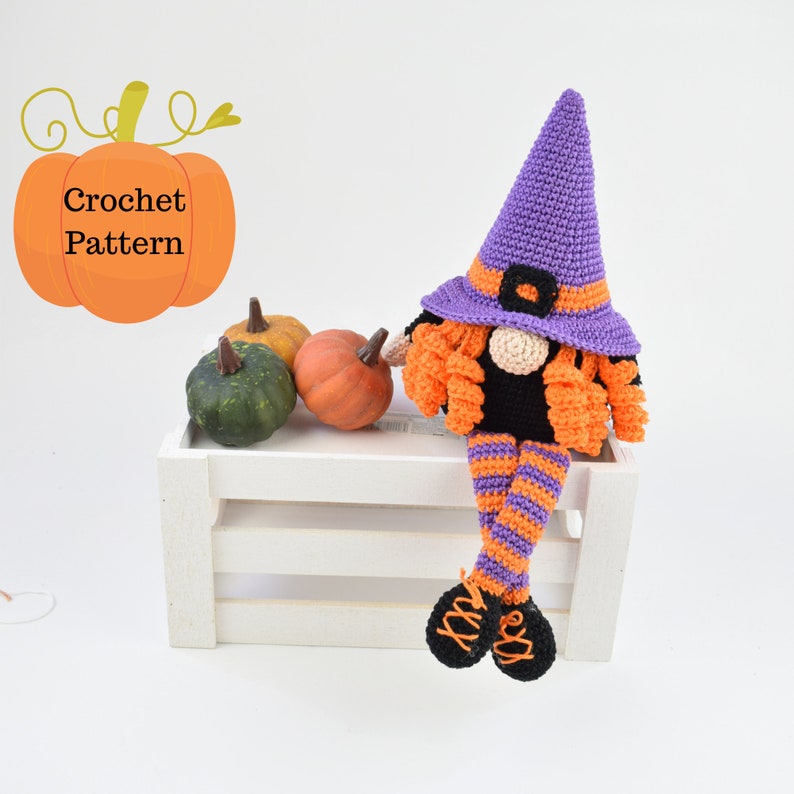May include: Crocheted Halloween witch gnome with purple hat, orange and black striped legs, and orange hair. The gnome is sitting on a white wooden crate with three small pumpkins in front of it.