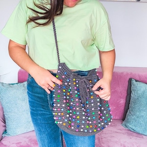 May include: A gray crocheted bag with colorful beads. The bag has a drawstring closure and a long strap.