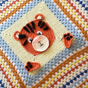 Peut inclure: Une couverture pour b&eacute;b&eacute; en crochet avec un motif de carr&eacute;s de grand-m&egrave;re color&eacute;s. La couverture pr&eacute;sente un visage de tigre en crochet et deux empreintes de pattes.