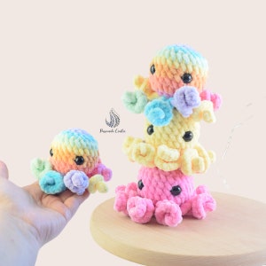 May include: A stack of three crocheted rainbow octopus plushies. The bottom octopus is pink, the middle is yellow, and the top is a light blue and pink ombre. A smaller rainbow octopus is in the foreground.