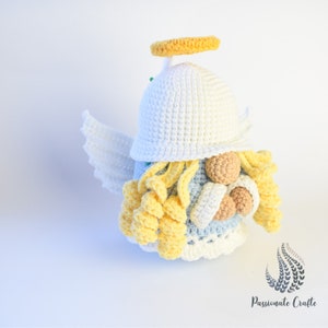 May include: A crocheted angel gnome with a white hat, yellow halo, and a blue and white beard. The gnome is wearing a white dress with a blue trim.