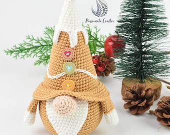 May include: A crocheted gingerbread gnome with a white hat and beard. The gnome has a brown body with colourful buttons and a white brimmed hat.