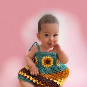 K&ouml;nnte beinhalten: Ein kleines M&auml;dchen tr&auml;gt ein geh&auml;keltes Kleid mit einem mehrfarbigen Muster aus Braun, Gelb und Gr&uuml;n. Das Kleid hat ein quadratisches Design mit einer Blume in der Mitte.