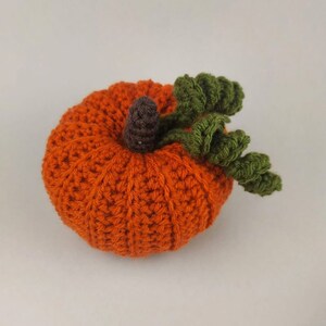 Puede incluir: Una calabaza naranja de ganchillo con hojas verdes y un tallo marrón.