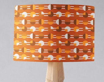 Può includere: Una lampada da terra con base a treppiede e un paralume a tamburo con un motivo geometrico in tonalità arancio, marrone e bianco.