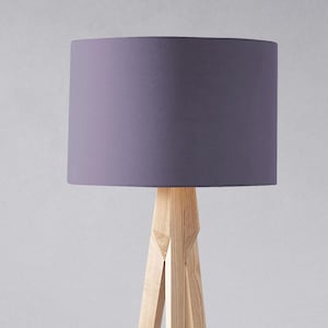 May include: A tripod floor lamp with a light purple fabric lampshade. The lamp has a natural wood finish.