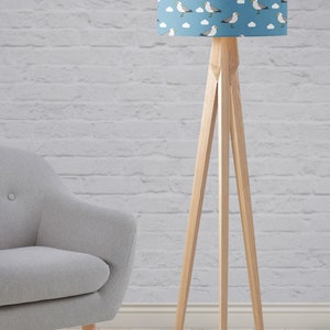 May include: A wooden floor lamp with a blue lampshade featuring a white seagull and cloud pattern. The lamp has a tripod base.
