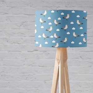 May include: A blue lampshade with a white and gray seagull pattern. The lampshade is on a wooden tripod stand.